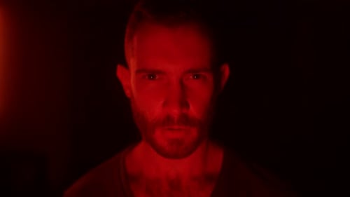 Un homme en colère, les yeux ouverts, se réveille en enfer en regardant la caméra avec fureur et rage, son visage illuminé par des flammes de feu