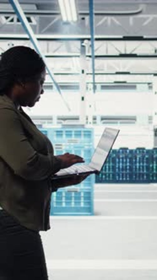 Vertical Video Technician with Laptop Walks Through Data Center Server Rows