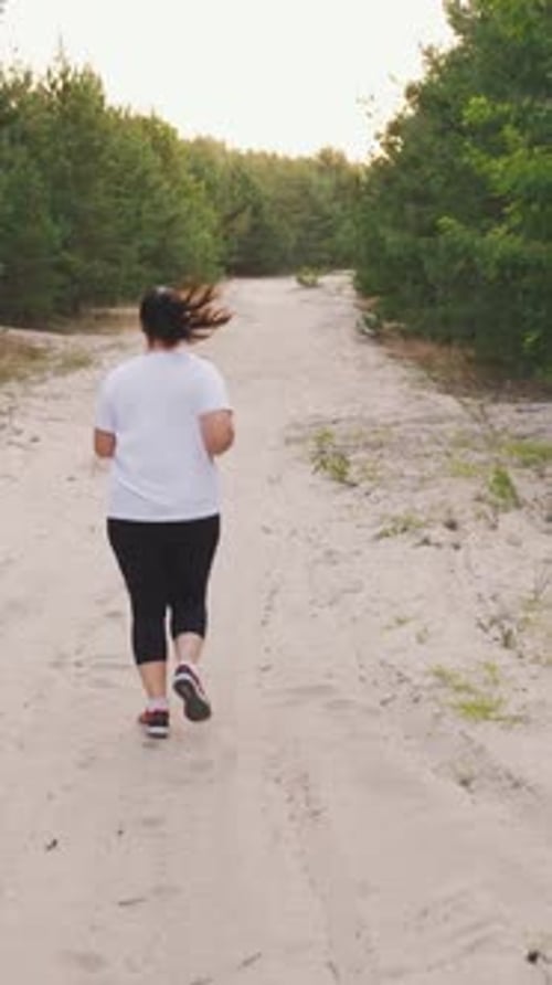 A Plump Unrecognizable Brunette Runs in a Beautiful Forest Plus Size Girl in Sportswear Runs Trains