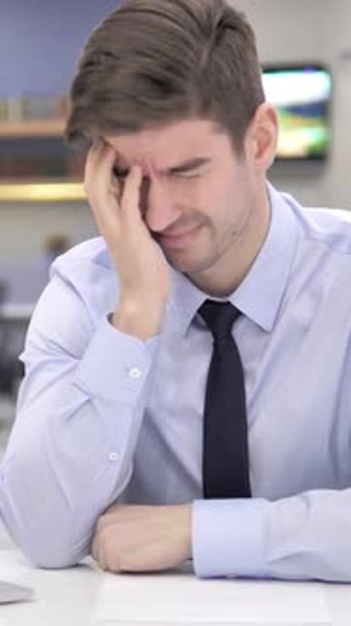 Worried Young Man Sitting at Desk with Headache