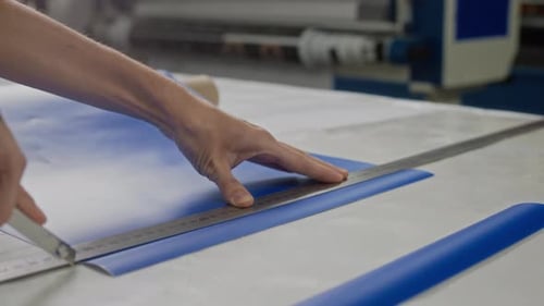 Close Up of Hand Cutting Blue Material with Ruler