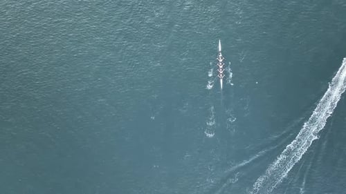 Tracking Aerial shot of rowers rowing down a river past boats.