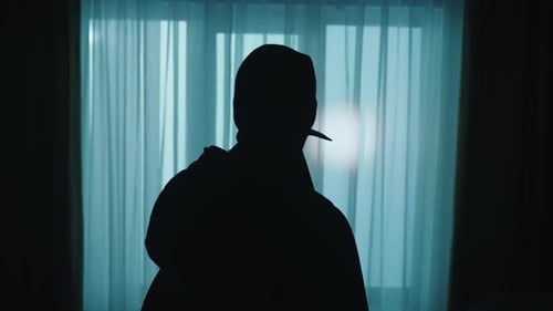 A Thief Looks Around in a Dark Apartment Using a Flashlight Close Up A Robber in a Balaclava with a