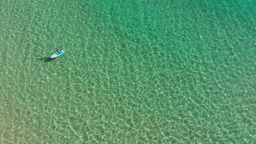 AERIAL: stand up paddle boarder is paddling along the coastline of portugal slowly tilting the camer