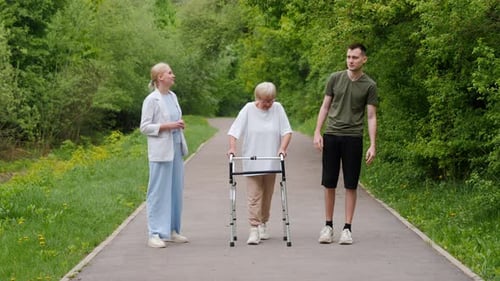 Middleaged Woman Young Man and Elderly Woman with a Walker Enjoying a Walk in a Green Park