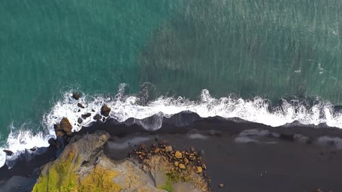 Top down aerial view of the black sand beach in southern Iceland, rocky coastline with waves splashi