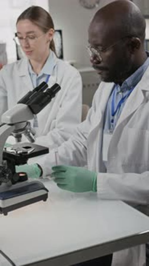 Scientists Analyzing Sample Under Microscope in Lab
