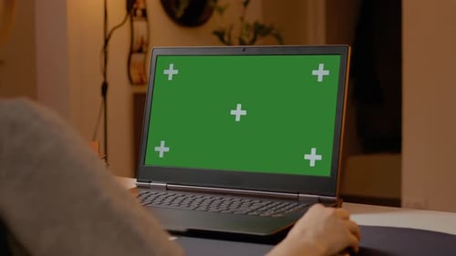 Woman working on laptop with green screen in home office environment