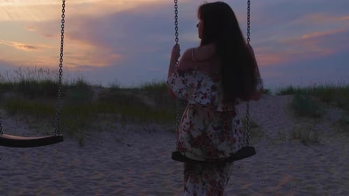 Young Pretty Woman Swings on a Swing Against the Background of Sand Grass