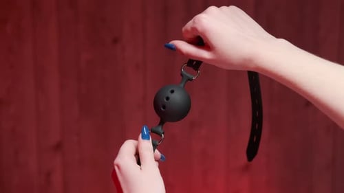 Sex toys for adults in a box. Close-up girl holding a black gag in her hands on a red background Sex toys for adults in a box. Close-up girl holding a black gag in her hands on a red background