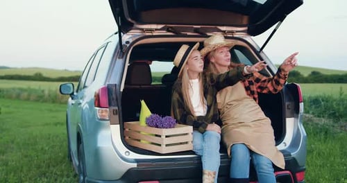 Woman and Girl Sitting in Car Trunk in Field