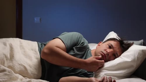 Schlafloser Mann, der nachts im Bett liegt und an Schlaflosigkeit leidet