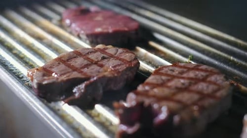 Chef preparing a delicious meal. Cooker frying pieces of juicy beef meat on grill. Steak grilled on