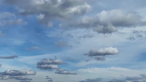 Clouds changing shape in the blue sky. Low angle view at the horizon with floating fluffy clouds.