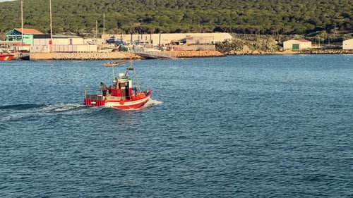 A boat glides gracefully over the waters of the Spanish coast, with a picturesque fishing village in