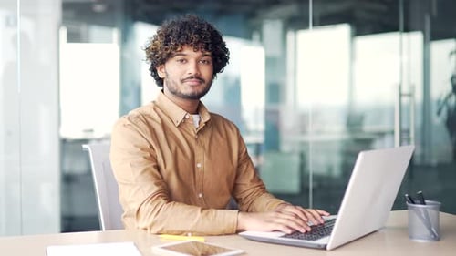 Portrait of a young successful handsome man sitting at a laptop at a workplace in a modern office.