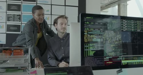 Two Engineers looking at Code on Computer Monitor in Office