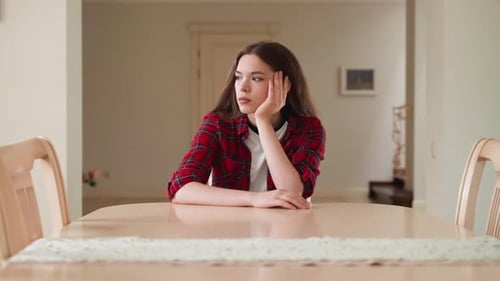Girl Sits Contemplatively at Table Inside Home