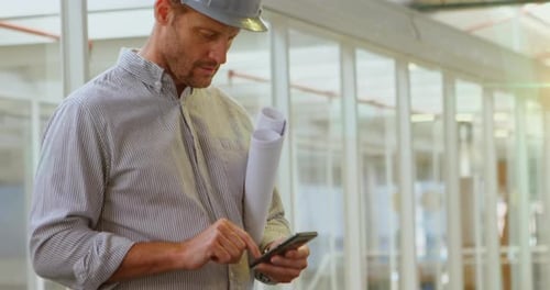 Man in Hardhat Using Phone and Holding Blueprints
