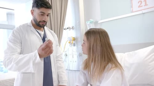 Diverse male doctor showing girl patient in hospital bed how to use asthma inhaler, slow motion