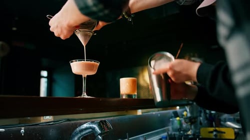 two young bartenders preparing alcoholic cocktails at the bar mixing ingredients working in pairs