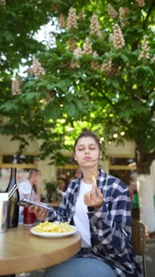 A Lovely Young Lady is Savoring French Fries on a Café Terrace During the Summer