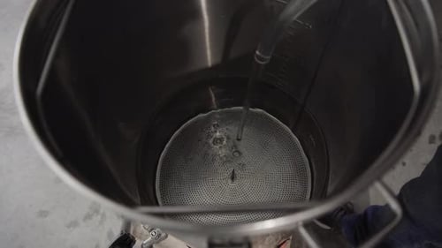 Água saindo de uma mangueira de plástico e enchendo dentro de uma grande panela ou chaleira de metal, fecho de alto ângulo