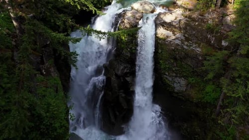 Majestic waterfall cascading down rocky cliffside found hidden deep in forest surrounded by trees.