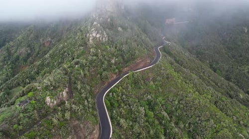 Aerial view of a mountain road surrounded by a green forest on a cloudy day