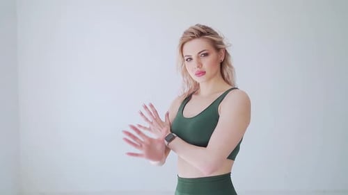 sporty woman in green sportswear approaches the window in a large white studio or hall. warm-up