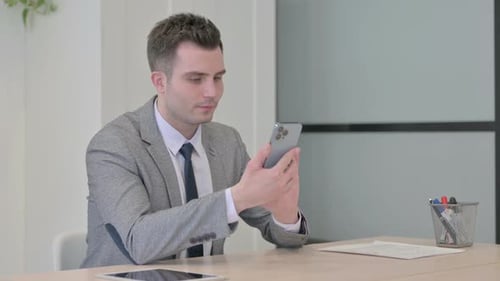 Young Businessman Browsing Internet on Smartphone in Office