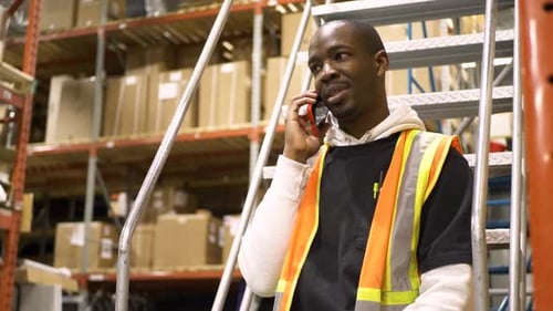 African american warehouse employee on smart phone taking a break from work