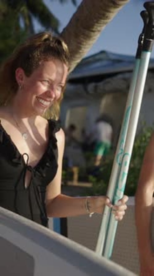 Woman Carries Surfboard and Paddle on Tropical Beach