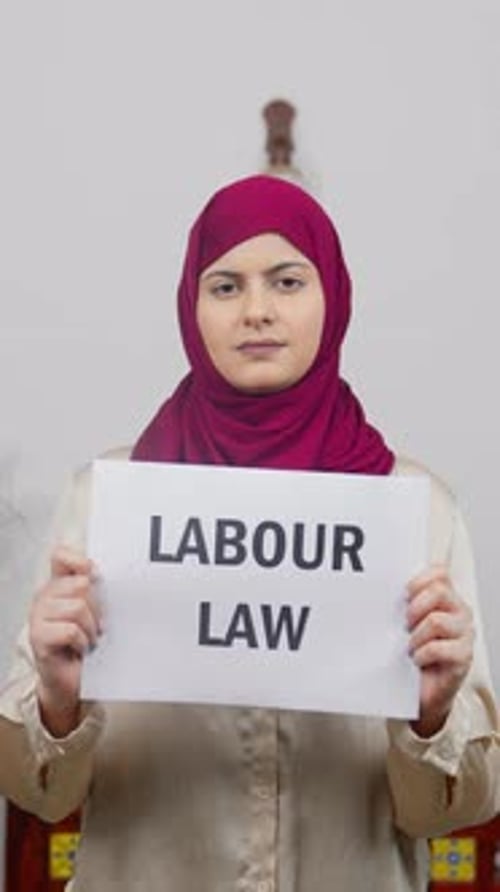 Vertical Video of Muslim Woman in Hijab Scarf standing with Labour Law Poster
