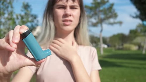 Woman Holds Inhaler in City Park, Close Up