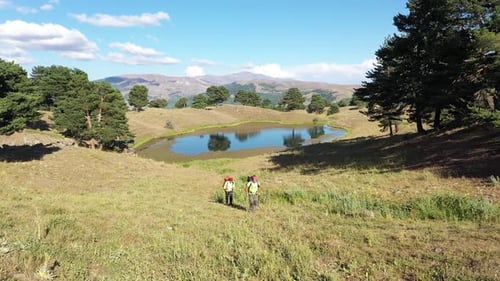 Aerial View Of Two Hiking Men Climbing Up Hill From Lakeside
