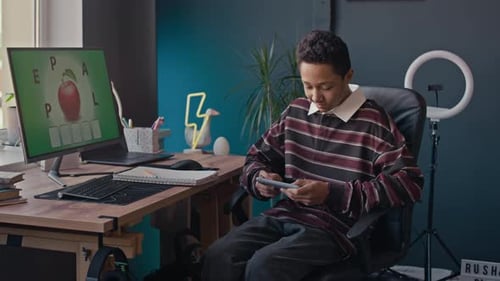 Teen plays game on his phone at desk