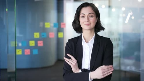 Portrait of a confident businesswoman in modern office with arms crossed smiling. Headshot of young
