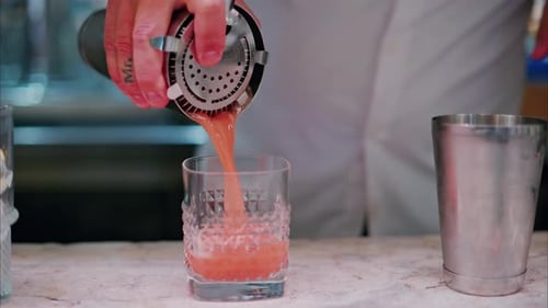 Barkeeper gießt an der Bar einen Orangencocktail in ein Glas