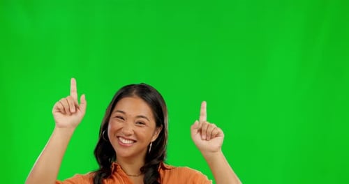Happy asian woman, pointing and advertising on green screen against a studio background