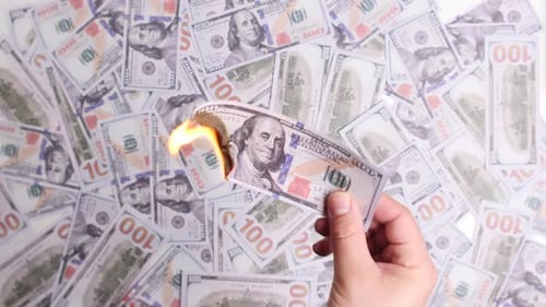 Hand haltend brennenden Hundert-Dollar-Schein vor Geldhintergrund
