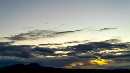 Golden sunrise over the Mojave Desert plains with mountains in silhouette as the cloudscape turns or