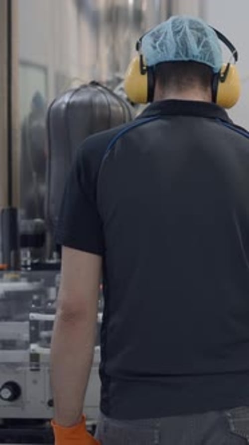Back View Of An Operator Wearing Hairnet And Headphones Working In A Beer Factory Medium Shot