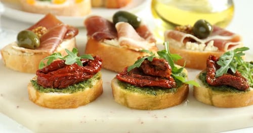 Délicieuses bruschettas au prosciutto et aux tomates séchées sur une table blanche. La caméra se déplace vers la droite