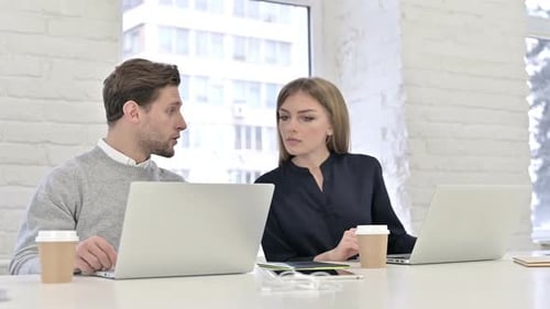Man and Woman Collaborating on Laptops in Office