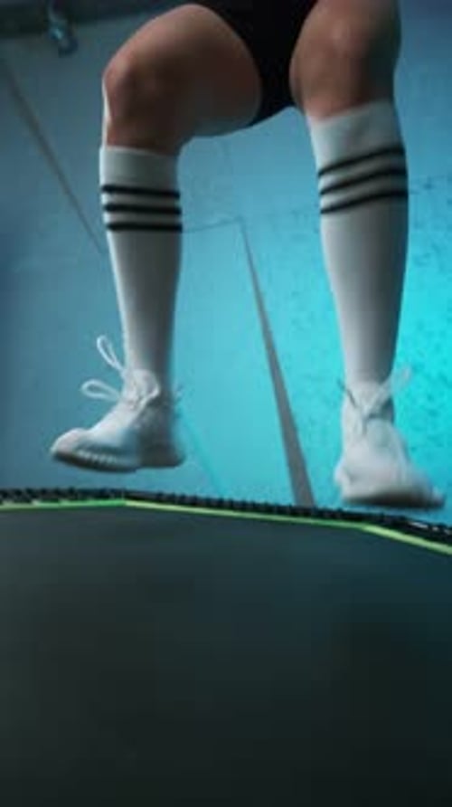 Close-up of legs of energetic young fitness girl in white sneakers jumping on mobile mini trampoline