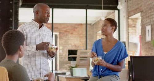 Happy african american colleagues discussing work and having lunch in creative office, slow motion