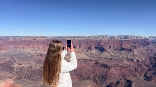 A Woman is Capturing Stunning and Breathtaking Views of the Grand Canyon While Using Her Smartphone