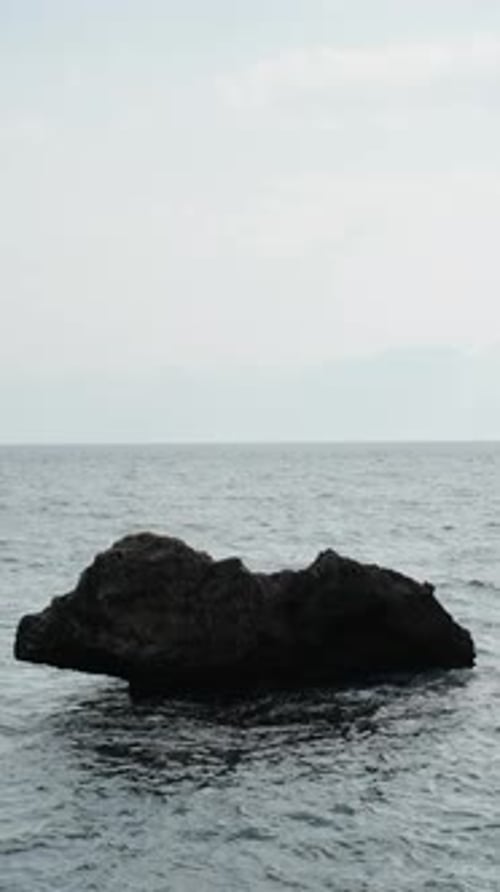 Vertical video. A view of the sea and a small rock protruding from the water, in slow motion.