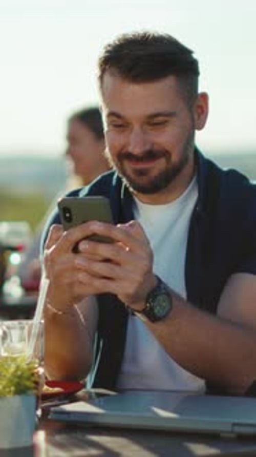 Smiling Man Using Cellphone at Outdoor Cafe